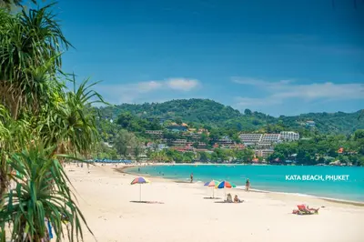 a beach with people sitting on the sand and the ocean at KK Karon Kata Boutique Hotel in Kata Beach