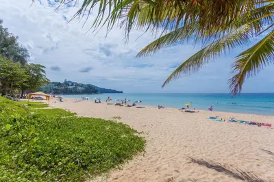 a beach with people sitting on the sand and the ocean at The Aristo by Holy Cow, studio, mountain view in Surin Beach