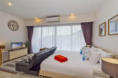 a bedroom with a bed and a chair and a television at Chic Condo by RESAVA in Karon Beach
