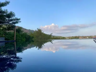 a large pool of blue water with trees and clouds at Infinity Pool Apartment at Viewpoint Villas in Nai Harn Beach