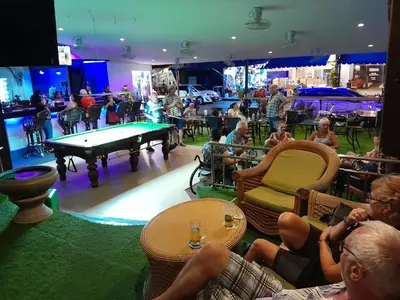 a group of people sitting in a bar with a pool table at Oasis Hostel & Bar in Karon Beach