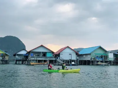 two people in a boat in the water with houses at Jamesbond Bungalow Koh Panyee in Ko Panyi