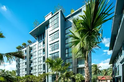 a tall white building with palm trees in front of it at Citygate Kamala Resort and Residence - Official Account in Kamala Beach