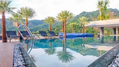 a swimming pool with palm trees and mountains in the background at Citygate Kamala Resort and Residence - Official Account in Kamala Beach