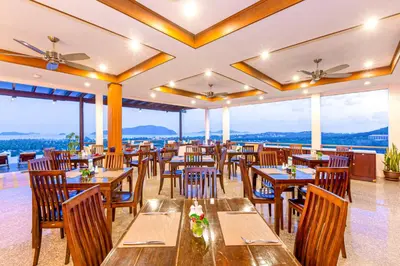 a restaurant with wooden tables and chairs and windows at The View Rawada Phuket in Rawai Beach