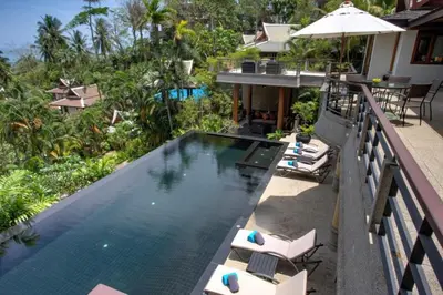 an infinity pool at a resort with chairs and an umbrella at Luxury 4 bedrooms Villa with Seaview Infinity Pool overlooking Surin Beach in Surin Beach