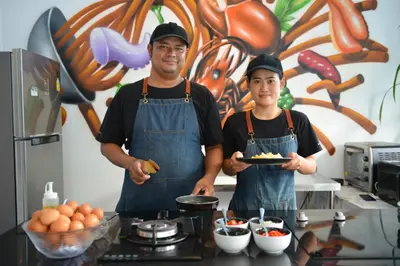 two men in a kitchen holding a plate of food at T2 Ao Nang Krabi in Ao Nang Beach