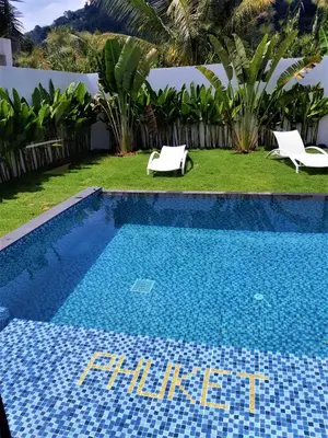 a blue swimming pool with two white chairs in a yard at Villa KHAO MANEE in Nai Yang Beach