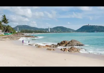 a beach with people walking on the sand and the ocean at Patong Karlssons Hotel in Patong Beach