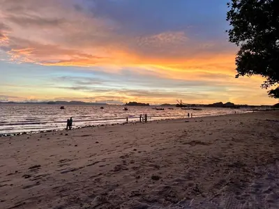 a group of people walking on the beach at sunset at At Thara Aonang in Ao Nang Beach