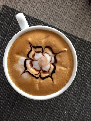 a cup of coffee with a flower painted on it at The Little Moon Residence in Patong Beach