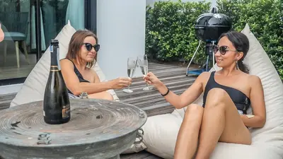 two women in bathing suits sitting at a table with a bottle of wine at Happy Family Villa in Phuket Town