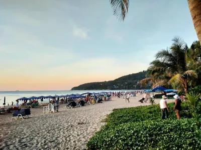 a crowd of people on a beach with blue umbrellas at PHADEE APARTMENT in Karon Beach
