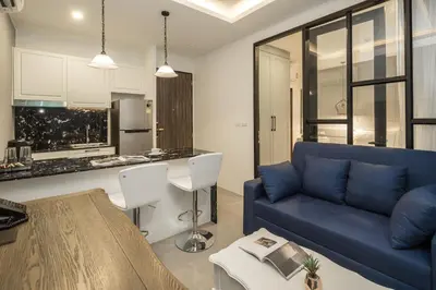a living room with a blue couch and a kitchen at Palmyrah Surin Beach Residence in Surin Beach