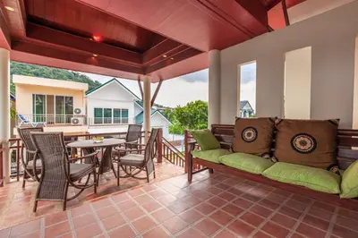 a porch with a green couch and a table and chairs at Sabai Villa Kata by RESAVA in Kata Beach