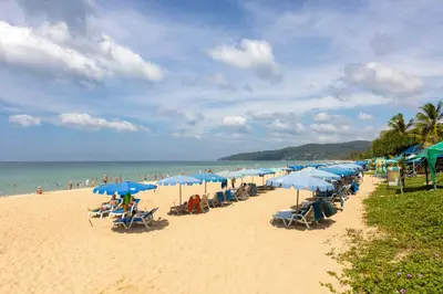 a beach with many blue umbrellas and people on it at Palmetto by Holy Cow, 2-BR, jungle view in Karon Beach