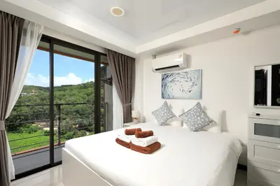 a bedroom with a white bed with a large window at NaiHarn Sea Condo, Top floor, Mountain View in Nai Harn Beach