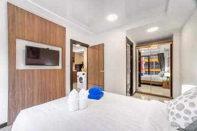 a bedroom with a white bed with a tv on the wall at SOLA Condo 1BR Tropical View NBC Nai Harn Nai in Rawai Beach
