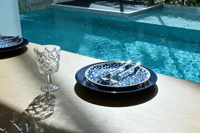 a table with plates and a wine glass next to a pool at Chomdao Maikhao in Mai Khao Beach
