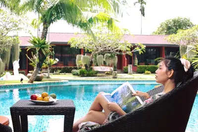 a woman sitting in a chair reading a book next to a pool at Mai Morn Resort SHA Plus in Phuket Town