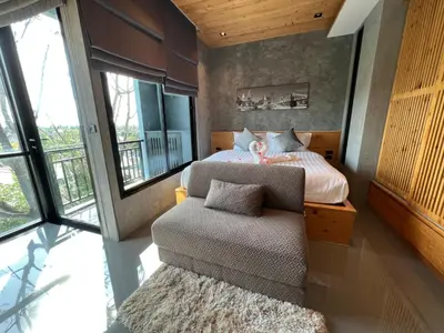 a bedroom with a bed and a chair and windows at Relife The Windy by VillaCarte in Rawai Beach