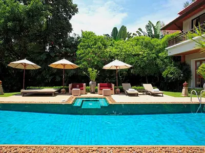 a swimming pool with chairs and umbrellas next to a house at Laguna Waters in Phuket Town
