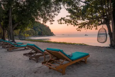 a row of lounge chairs on a beach at The Mooring Resort in Panwa Beach