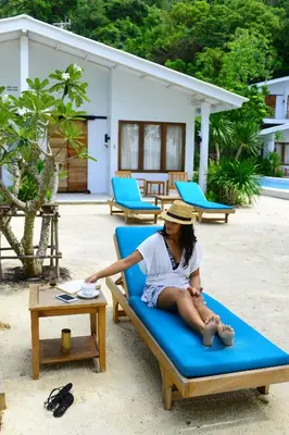 a woman sitting on a lounge chair on a beach at The Mooring Resort in Panwa Beach