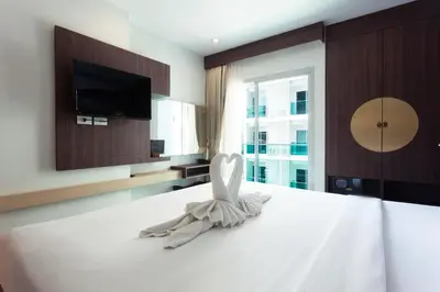 a bedroom with a bed with white sheets and a tv at The AIM Patong Hotel in Patong Beach