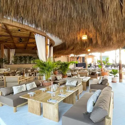 a restaurant with couches and tables and a straw roof at Arinara Beach Resort Phuket - SHA Extra Plus in Bang Tao Beach