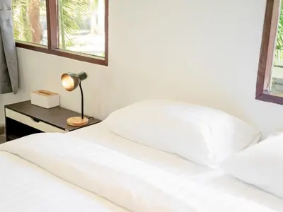 a bed with white sheets and a lamp on a table at Sand Beach Bungalow in Klong Muang Beach