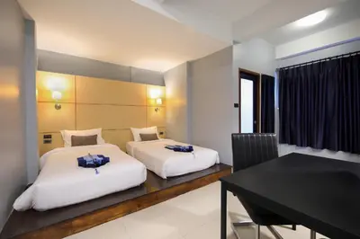two beds in a room with a table and a desk at Montree Phuket Hotel in Phuket Town