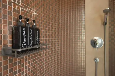 a bathroom with a shelf with bottles on a tiled wall at Queen Palm Villa in Rawai Beach