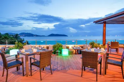a patio with tables and chairs and a view of the ocean at Zenmaya Oceanfront Phuket, Trademark Collection by Wyndham in Patong Beach