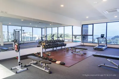 a gym with cardio equipment in a building with windows at 2-Bedroom Apartment at Calypso Garden Residences in Rawai Beach