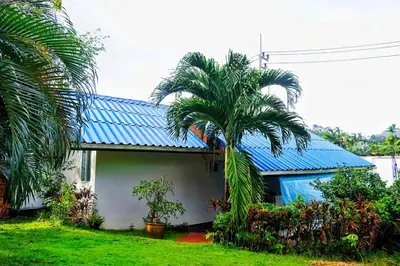 a house with a blue roof and two palm trees at Kingsacre in Nai Yang Beach