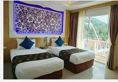 two beds in a hotel room with a window at Lucky Sun Patong in Patong Beach