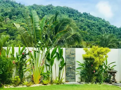 a garden in front of a fence with mountains in the background at Villa MAI MEE PAN HA 3 bedrooms in Nai Yang Beach