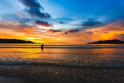 a person standing on the beach at sunset at Anona Beachfront Phuket Resort-SHA EXTRA PLUS in Patong Beach