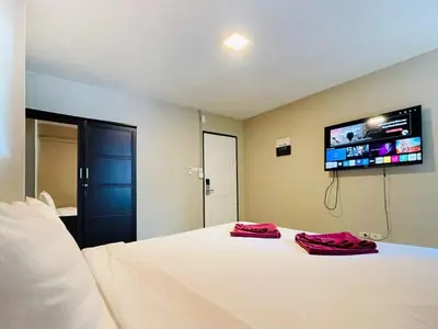 a bedroom with a white bed with a flat screen tv on the wall at Breakers Hotel Rawai in Rawai Beach