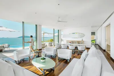 a man walking in a living room with white furniture at COMO Point Yamu, Phuket in Ban Pa Khlok