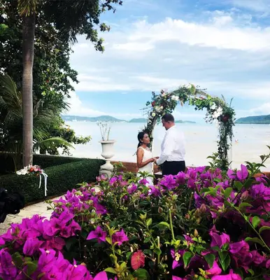 a bride and groom standing under an arch with flowers at Royal Thai Villa Phuket - SHA Extra Plus in Rawai Beach