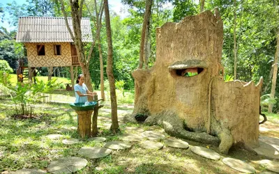 a woman standing in front of a tree stump with a house at Treehouse Holidays-Family house in Ko Yao Noi