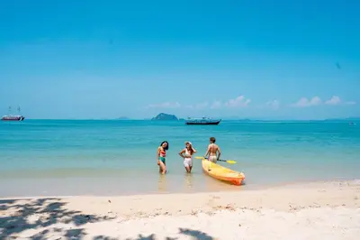 three people standing on a beach with a surfboard at Royal Yao Yai Island Beach Resort in Ko Yao Yai