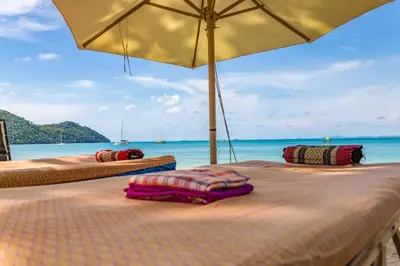 two beds on a beach with an umbrella at Royal Yao Yai Island Beach Resort in Ko Yao Yai