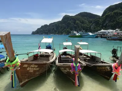 three boats are docked in the water on a beach at Coco's Guest House in Phi Phi Don