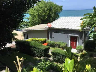 a house with a red door and the ocean in the background at Koh Sirey Beachfront Pool Villa - 2 Bedrooms House in Phuket Town