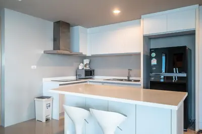 a kitchen with white cabinets and a counter with white chairs at The Ark at Veloche Group by Lofty in Karon Beach