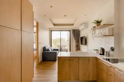 a kitchen with wooden cabinets and a living room at The Aristo 2 Condo Surin Beach in Surin Beach