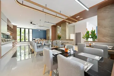 a dining room with tables and chairs and a kitchen at Grace Patong Hotel in Patong Beach